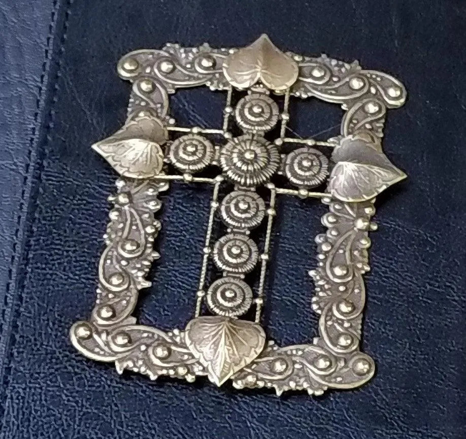Closeup of ornate metal cross with floral details on a dark leather Holy Bible cover