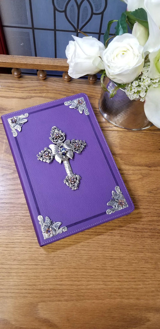 Large print purple jeweled Bible with ornate silver cross cover, displayed on wooden table