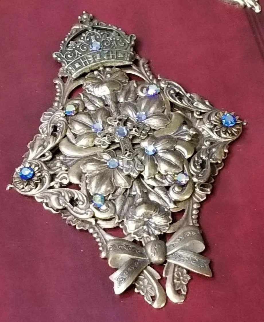 Jeweled Bible cover with ornate silver floral and cross design, blue gemstones, on burgundy background.