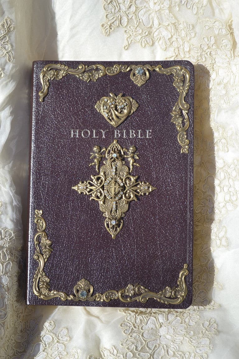 Jeweled maroon Holy Bible with ornate gold metal cross and decorative accents on lace