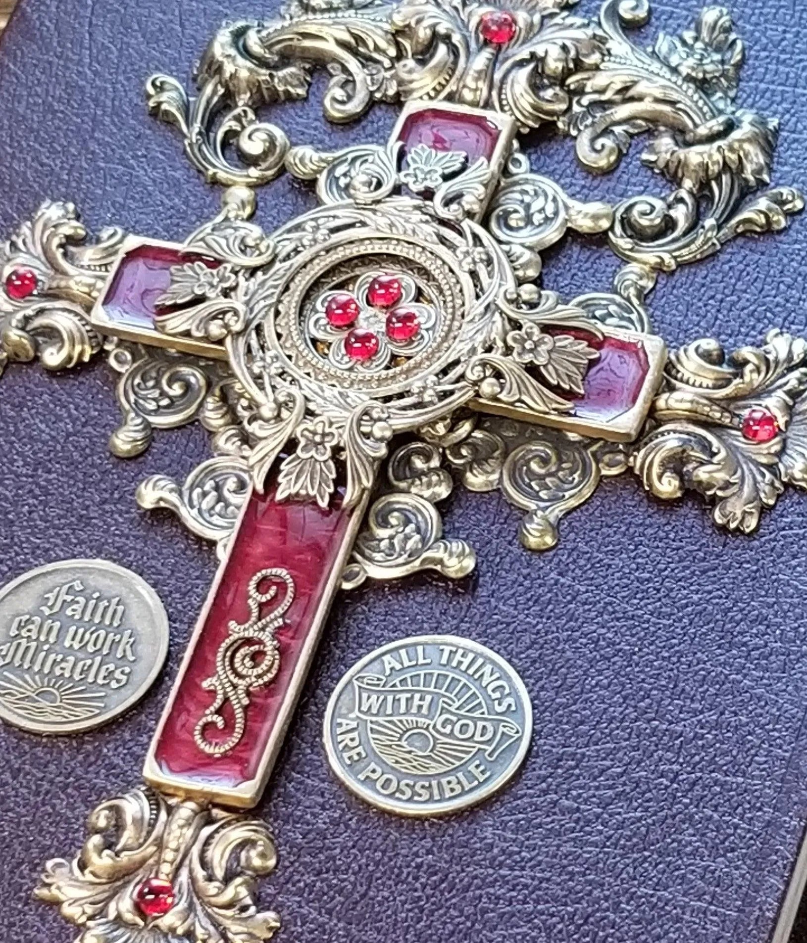 Jeweled ornate cross with red gems on Bible cover, surrounded by faith-themed metal coins.