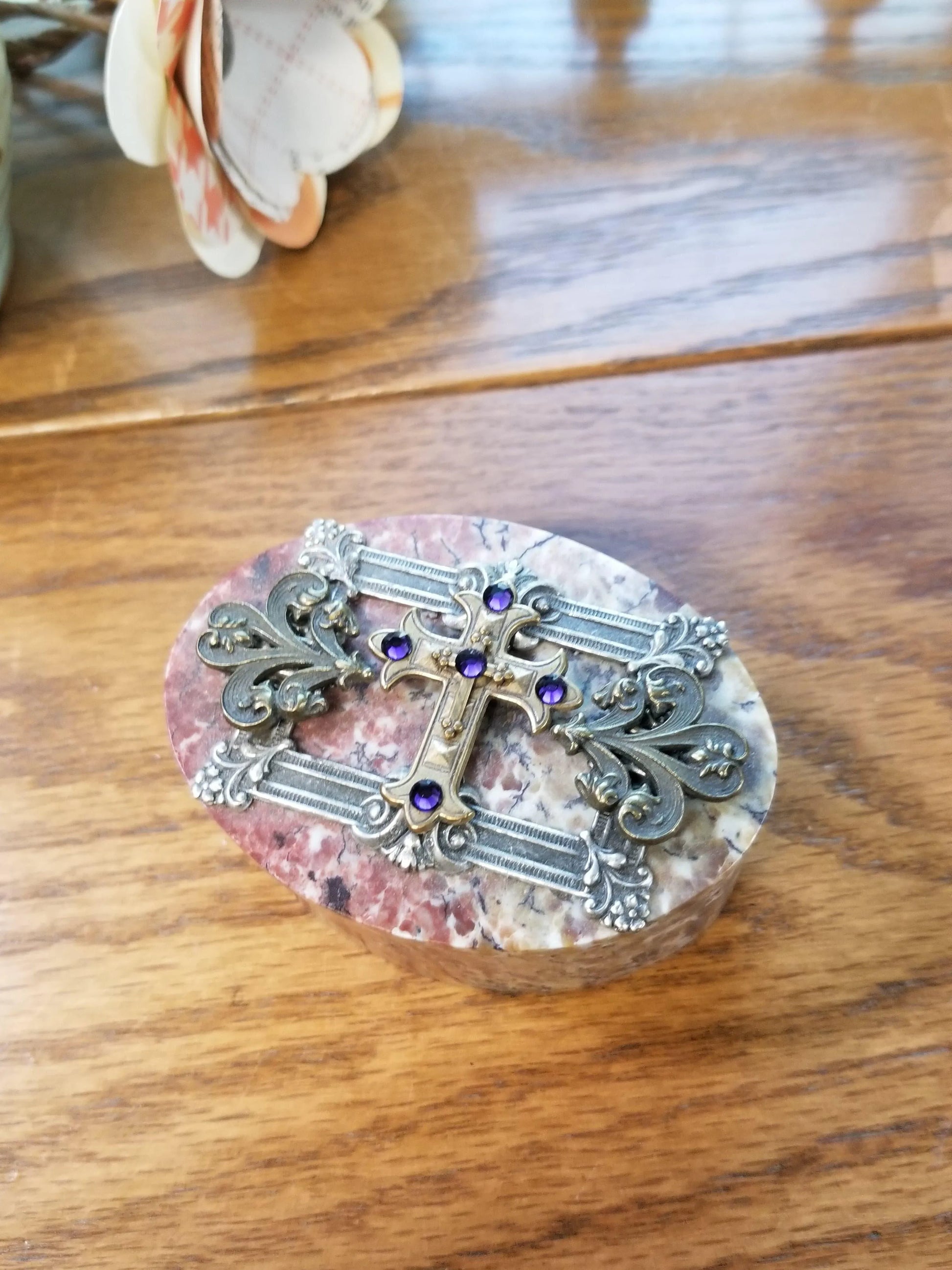 Ornate jeweled keepsake box with silver cross and purple gemstones on marble lid