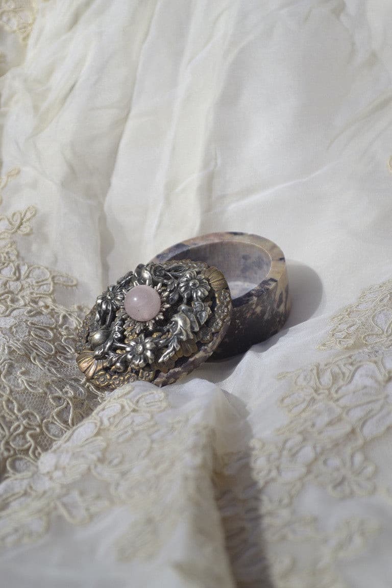 Open soapstone keepsake box with ornate jeweled floral metallic lid on lace fabric