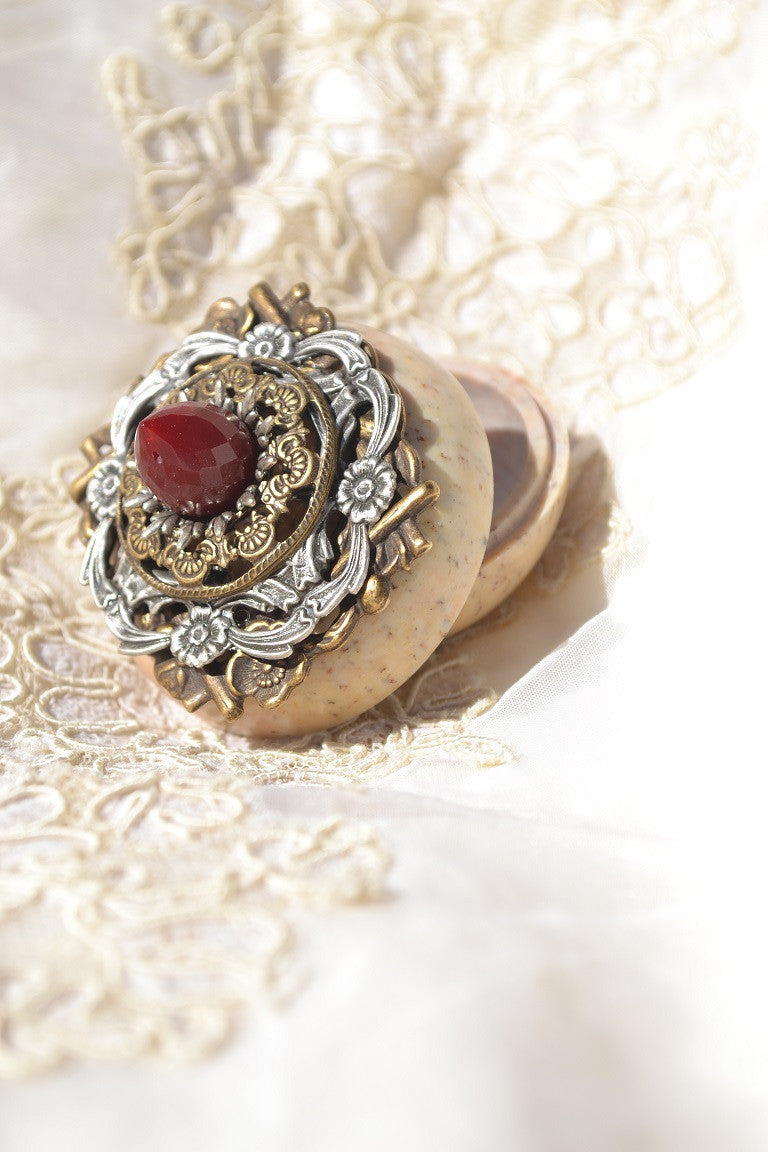 Jeweled soapstone keepsake box with ornate lid and red gemstone, open on lace fabric