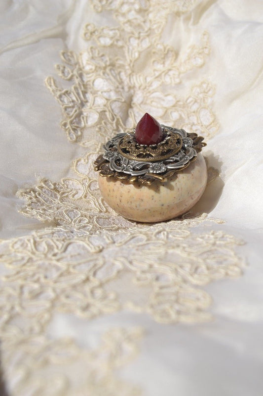 Ornate soapstone keepsake box with jeweled red gemstone lid on embroidered fabric