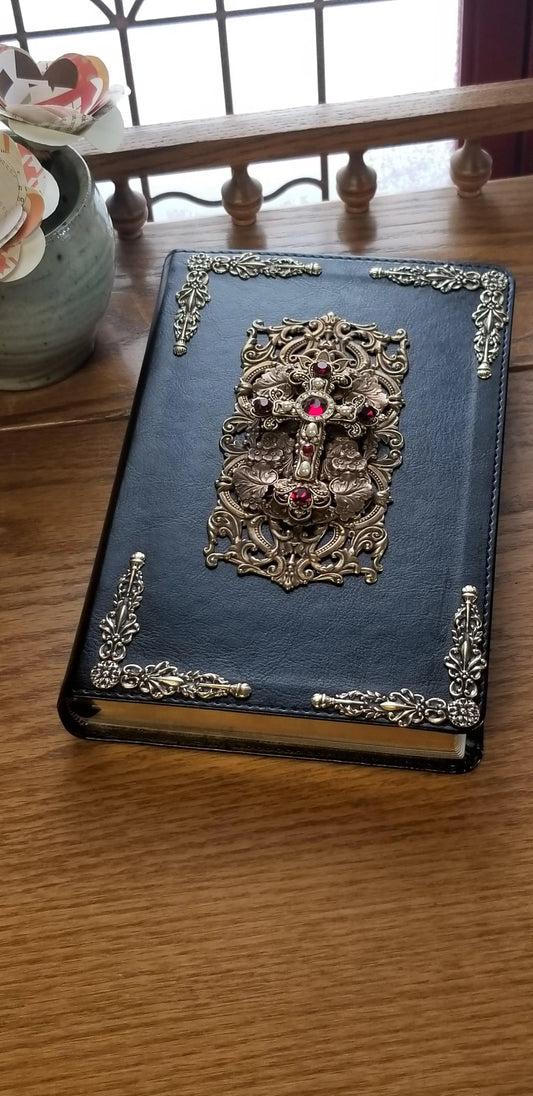 Black leather jeweled Bible with gold ornate cross and red gemstones on wooden table