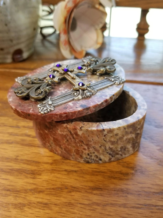 Open jeweled keepsake box with ornate cross and purple gemstones on lid, on wooden table