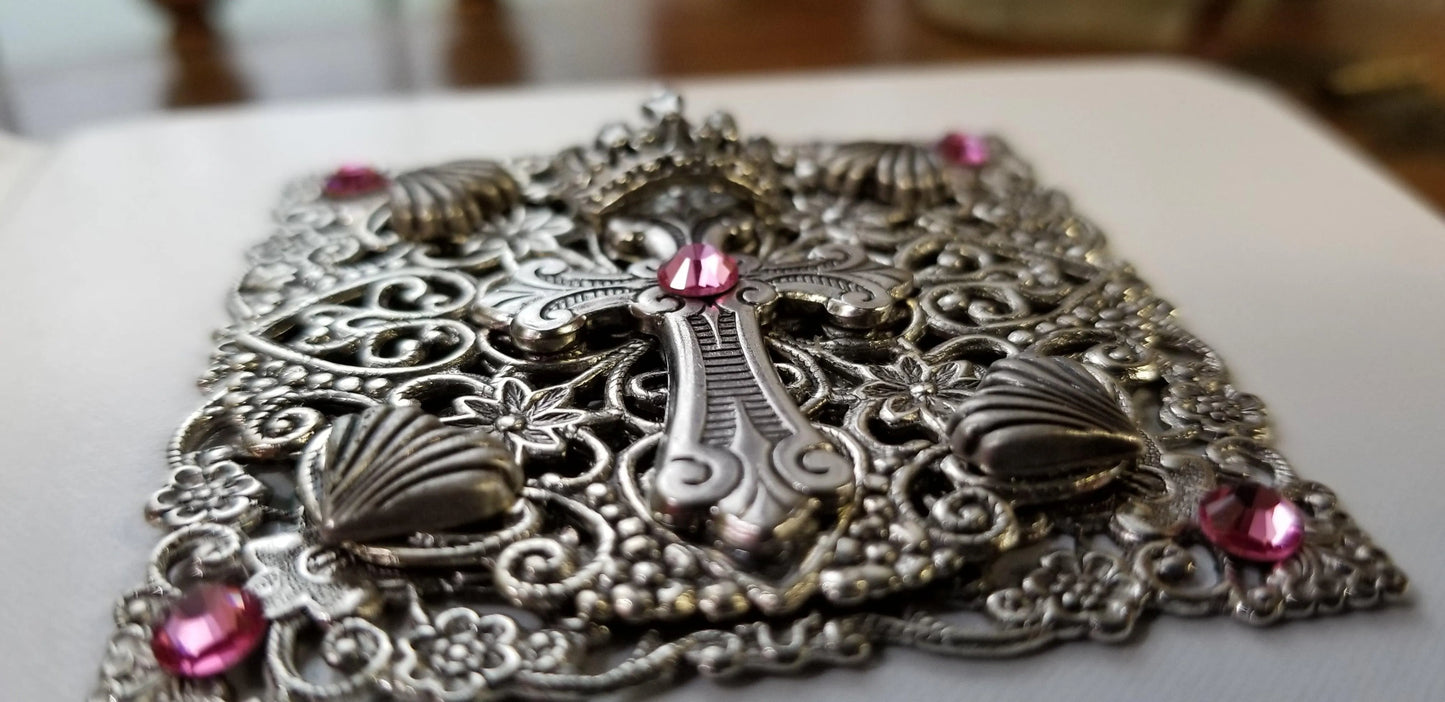 Close-up of ornate jeweled baby Bible cover with silver cross and pink gemstones