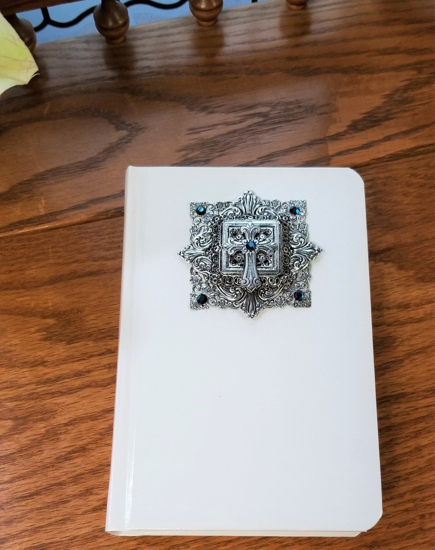 White journal with ornate silver cross and blue gemstones, faith-based keepsake