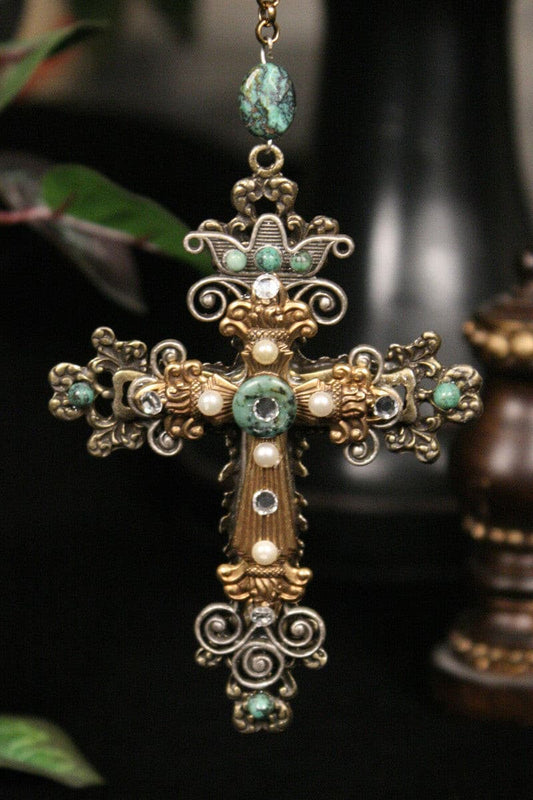 Gold cross ornament with green stones, pearls, and ornate filigree design on black background