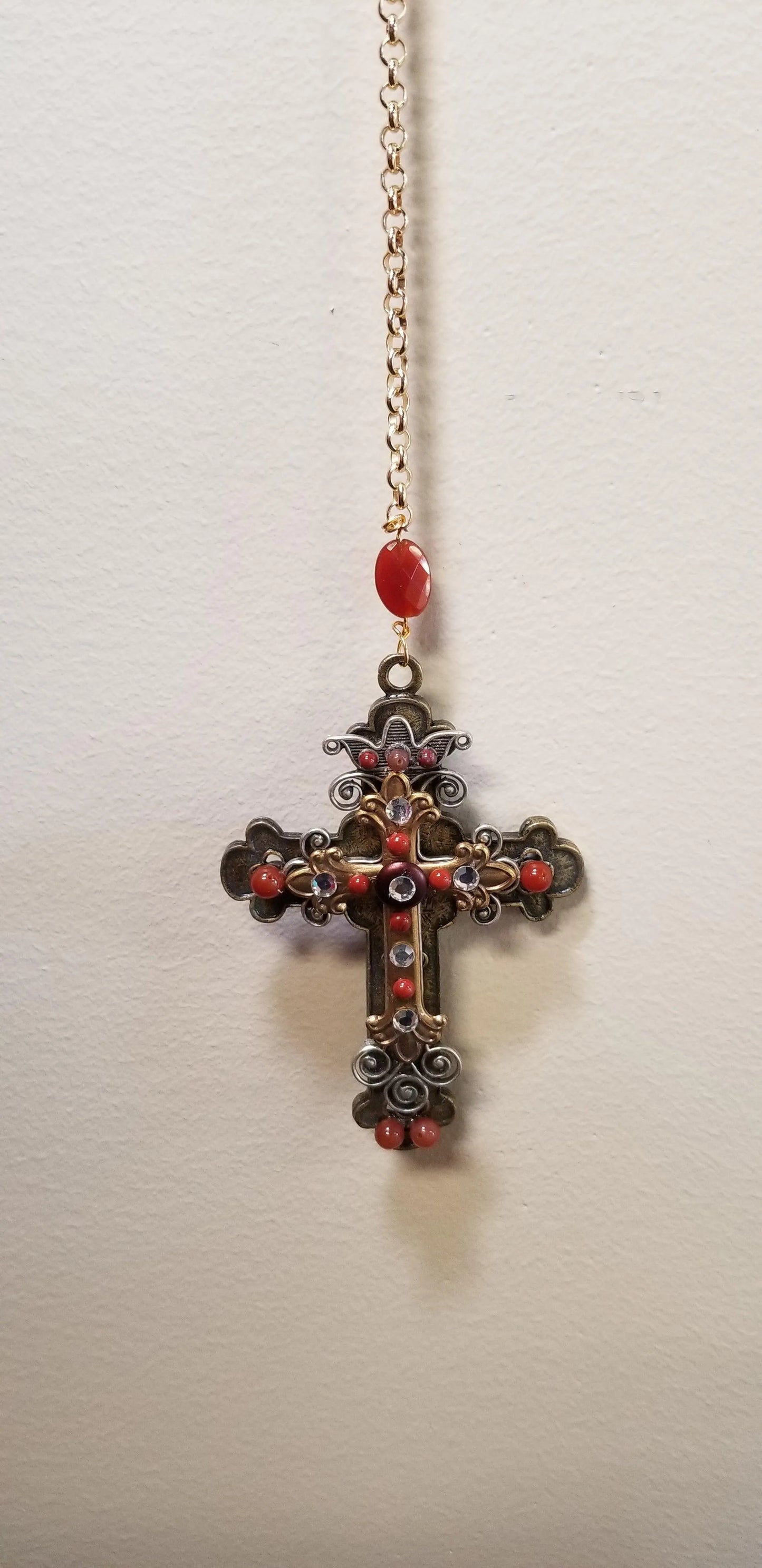 Ornate gold cross ornament with red stones and crystals on a hanging chain